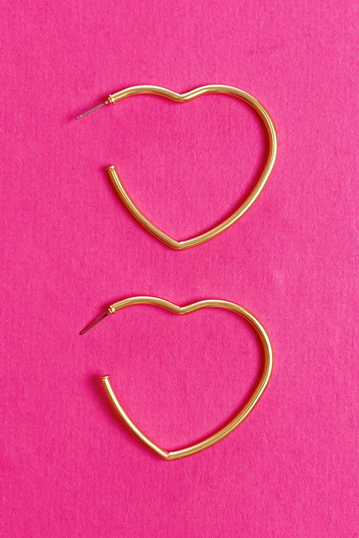 gold heart hoop earrings displayed on pink background