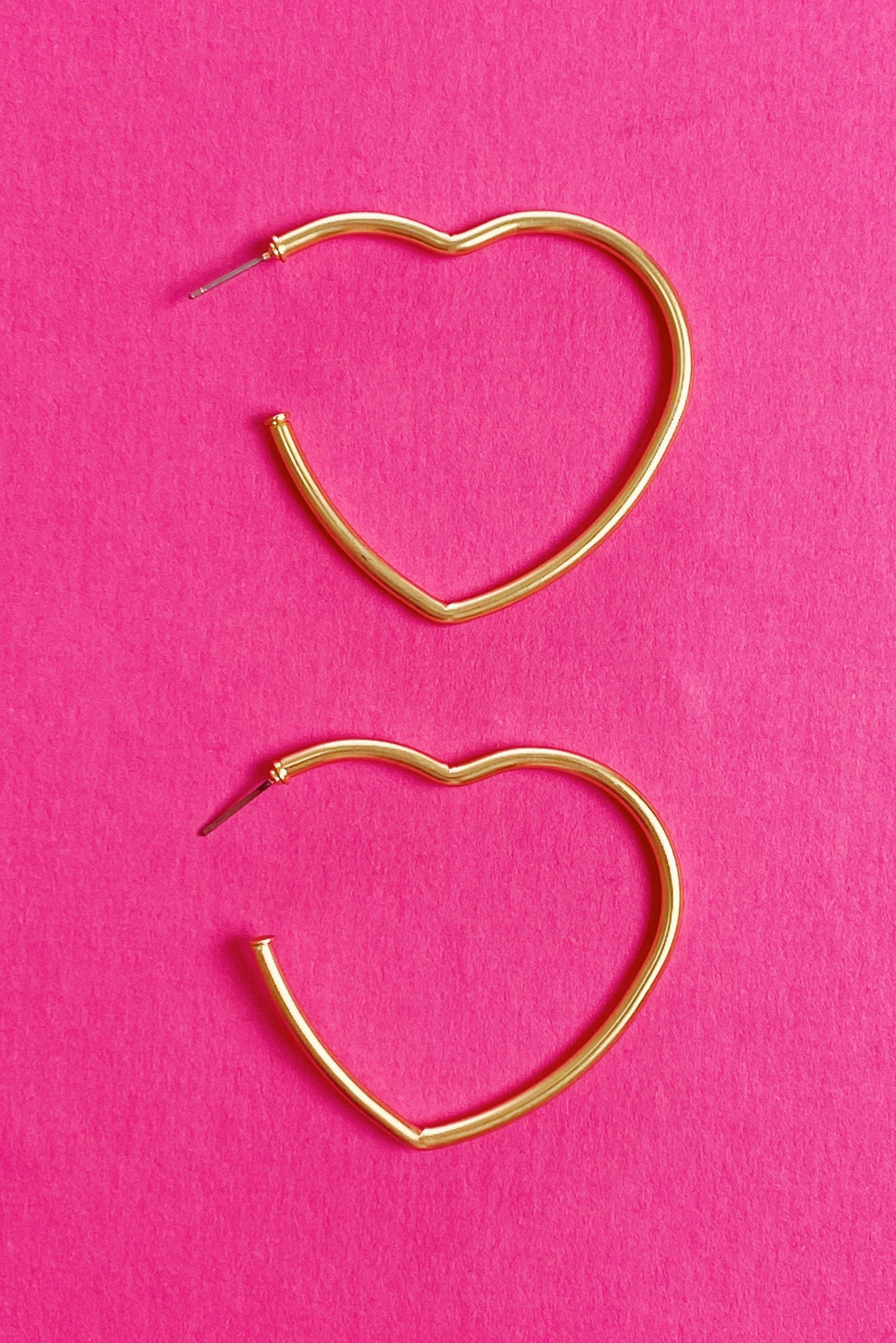 gold heart hoop earrings displayed on pink background