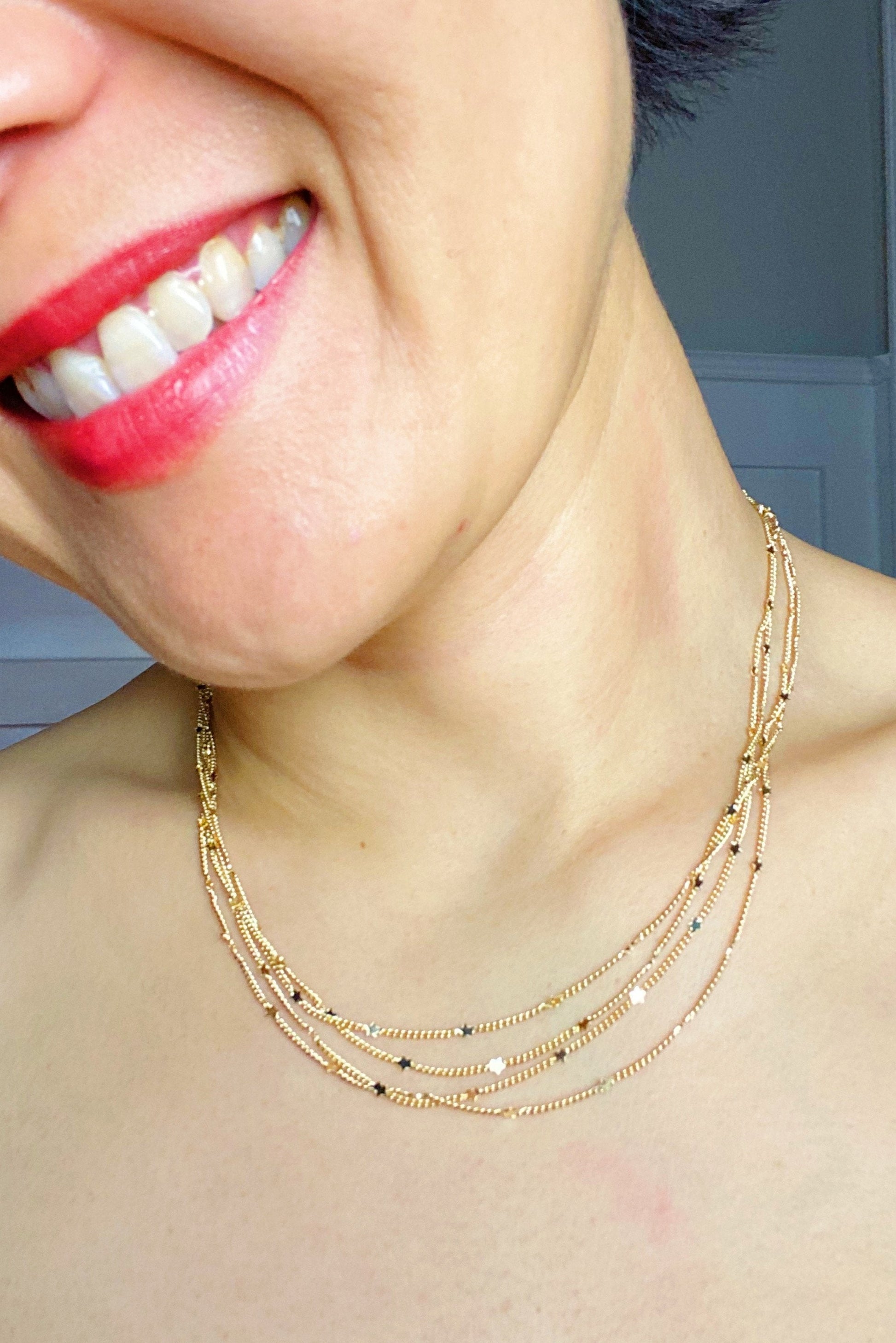 Woman wearing layered gold chain necklace with tiny star charms 