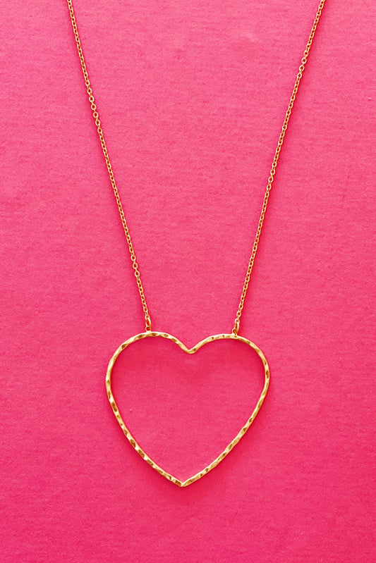 gold chain necklace with hammered heart pendant displayed on hot pink background