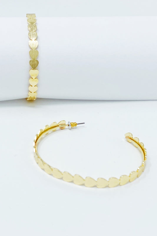 Gold hoop earrings with small hearts all around displayed on white jewelry holder